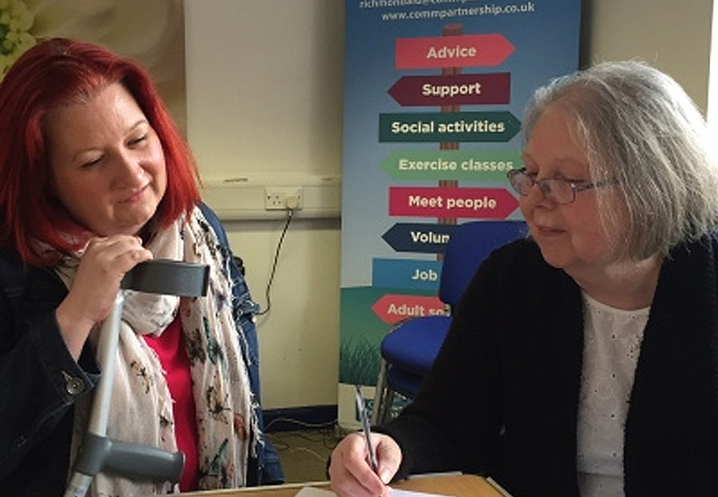Advisor supporting a woman with a walking aid during a benefit advice session.