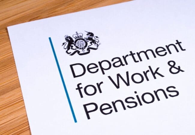 A document on a wooden surface displays the UK government crest above the text Department for Work & Pensions, relating to the Timms Review of PIP.