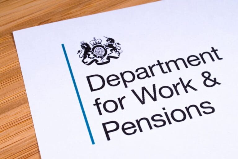 A document on a wooden surface displays the UK government crest above the text Department for Work & Pensions, relating to the Timms Review of PIP.