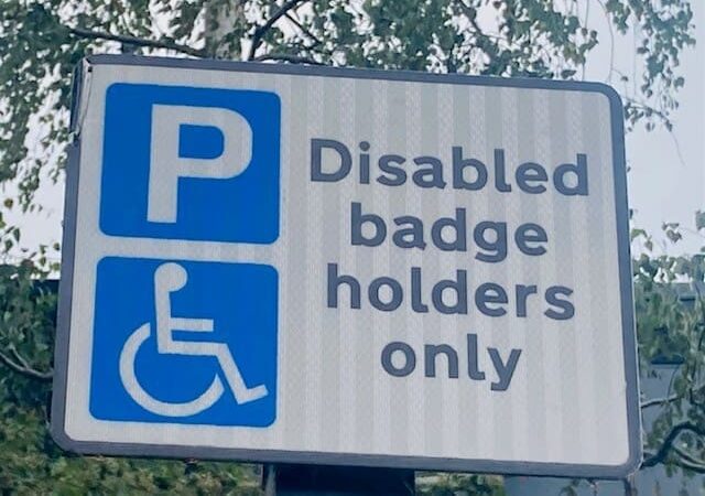 Blue Badge Parking sign with the wheelchair symbol and text reading Disabled badge holders only against a background of trees, clearly indicating accessible parking for Blue Badge permit holders.