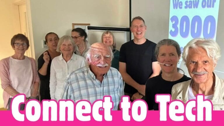 A group of older adults smiles in a classroom with a projector screen reading We saw our 3,000 Attendances. Text over the image says Connect to Tech in bold pink and white letters, celebrating this inspiring tech event.